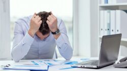 Stressed businessman with papers and charts sitting at table in office
